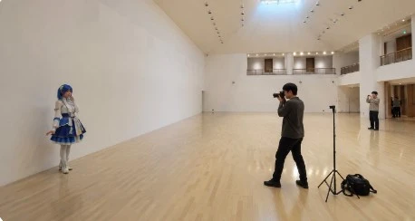 白いスタジオで青い衣装のコスプレイヤーを撮影するカメラマン
