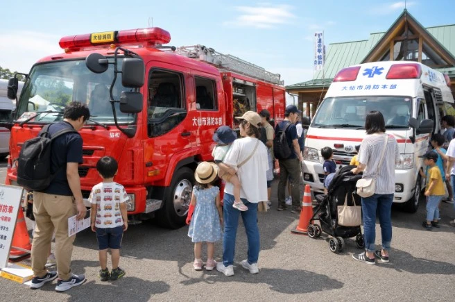 消防車と救急車を間近で見学する家族連れのイメージ