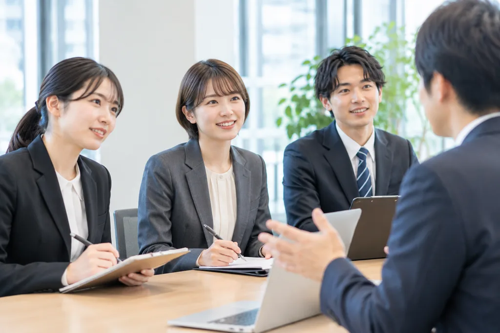 オフィスのテーブルで説明を聞きながらメモを取る3人