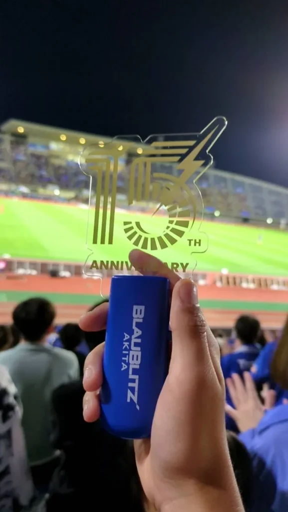 スタジアムでブラウブリッツ秋田の17周年記念デザインを掲げる手元