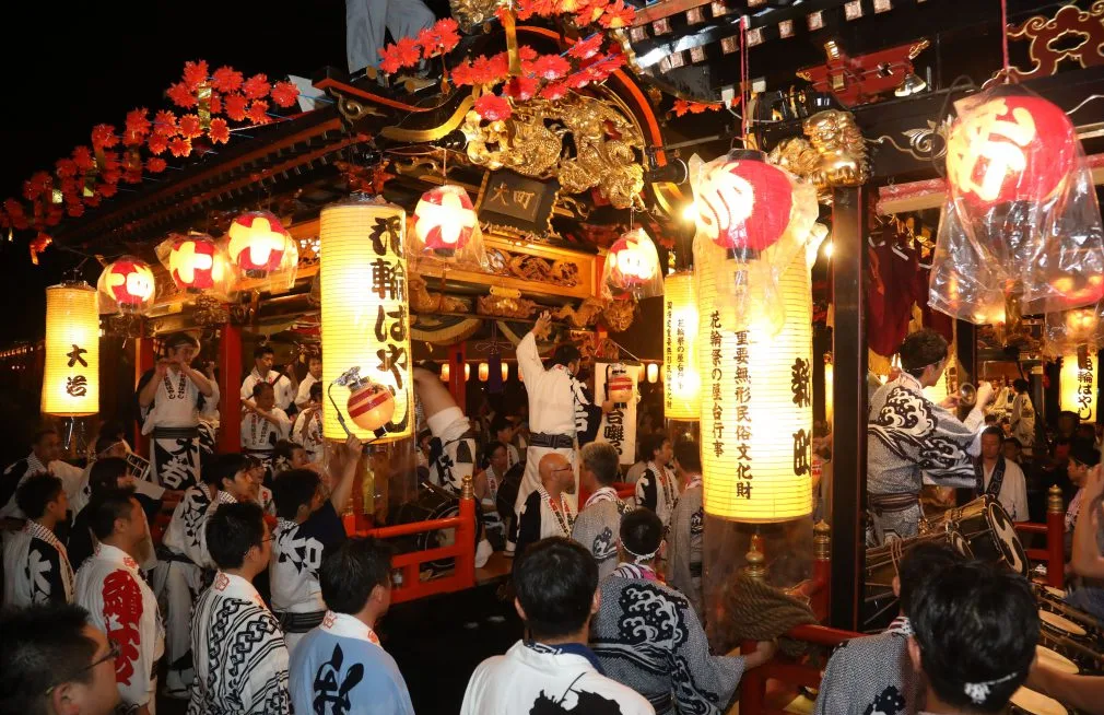 赤い提灯や金色の装飾が施された花輪ばやしの屋台と、周囲で祭りに参加する人々