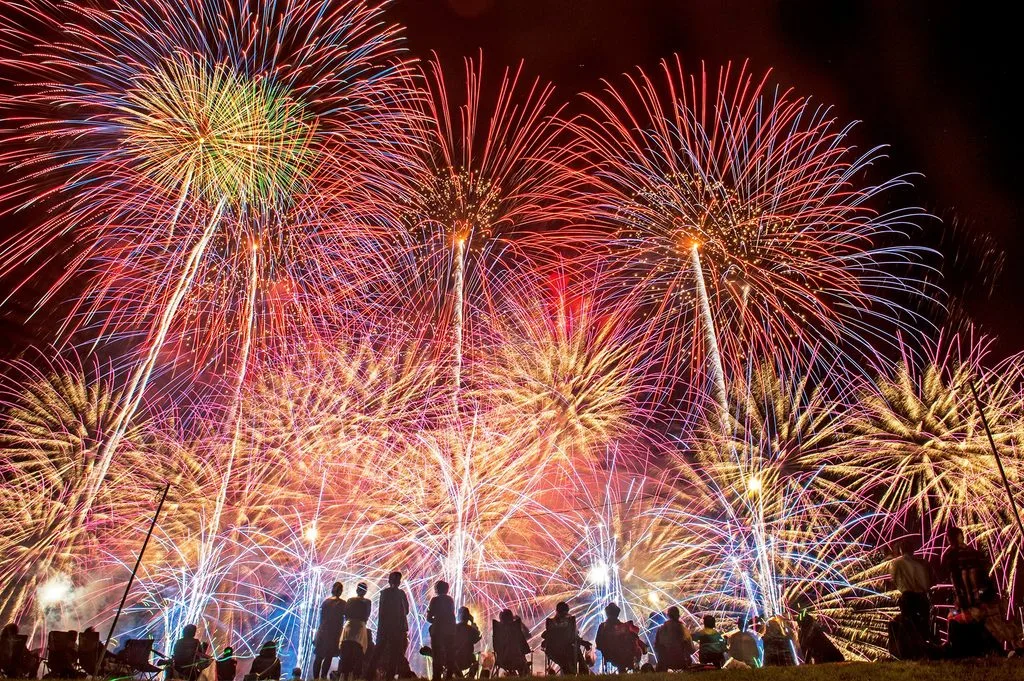 観客の頭上に広がる赤や金色の大規模な打ち上げ花火