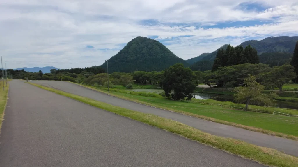 山と川に囲まれた芝生と舗装路のある河川敷