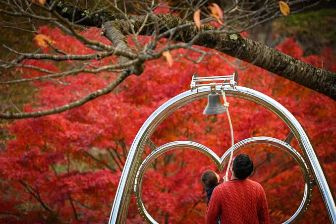 赤く色づいた紅葉を背景にきみまちの鐘を鳴らす人たち