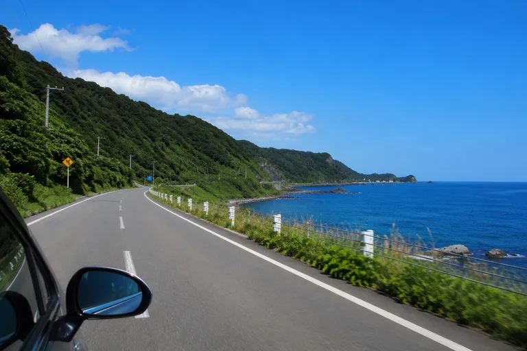 青い日本海に沿って続く海岸道路を車で走る様子