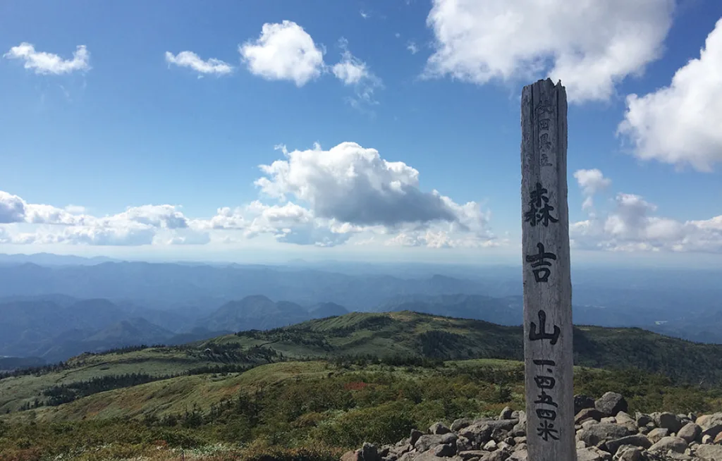 標高1454mと書かれた森吉山山頂の標柱と周囲の山並み