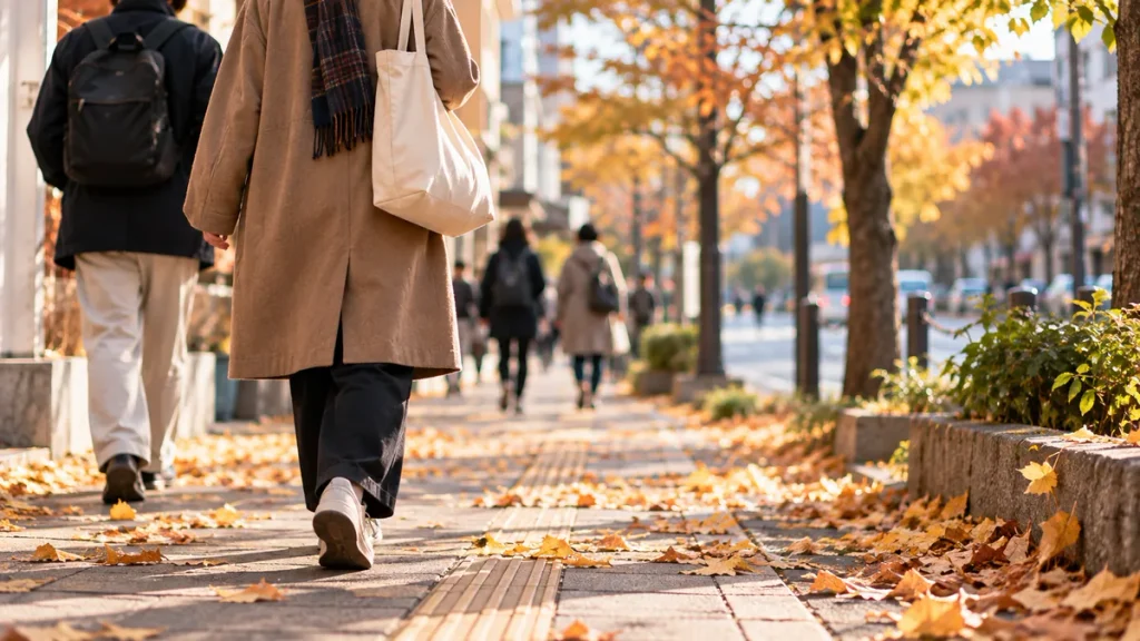 黄色やオレンジ色の落ち葉が広がる秋の街路を歩く人々