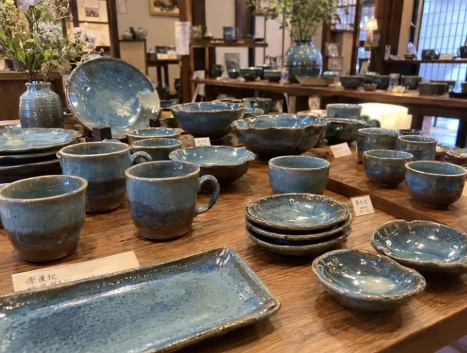 木製の展示台に楢岡焼特有の青みのある皿やカップ、器が並ぶ画像