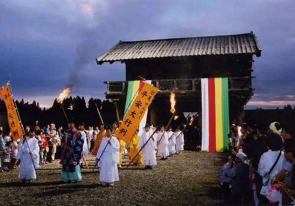 夕暮れの払田柵跡の復元門前でたいまつと旗を持って進む行列
