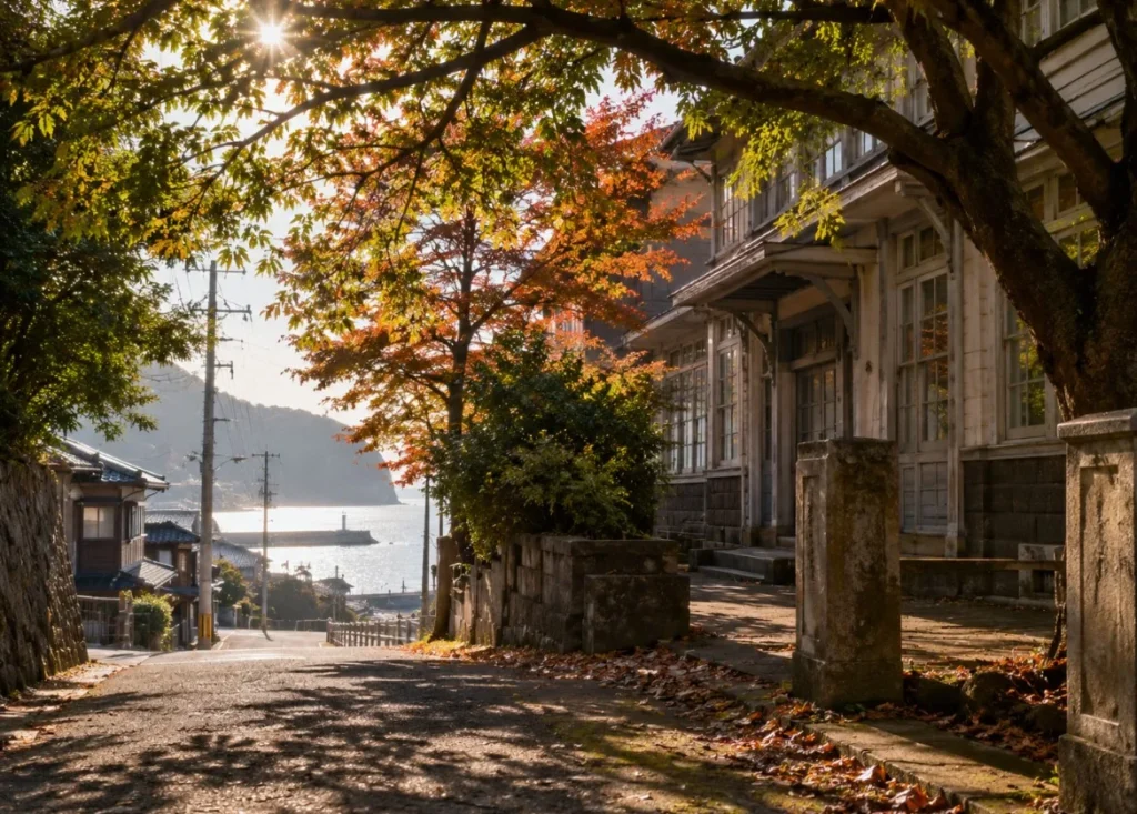 紅葉した街路樹の下を海へ向かって延びる坂道と古い建物のある町並みのイメージ