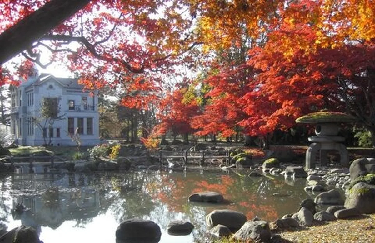紅葉に囲まれた池と白い洋館が水面に映る旧池田氏庭園