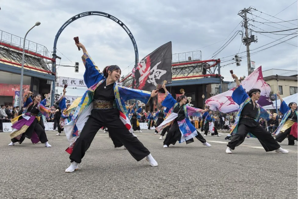 色鮮やかな衣装の踊り手が旗を背景に道路でよさこいを踊る様子